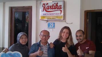 Un groupe de personnes se tient devant un bâtiment sur lequel est apposée une enseigne indiquant « Kartika Homestay ».