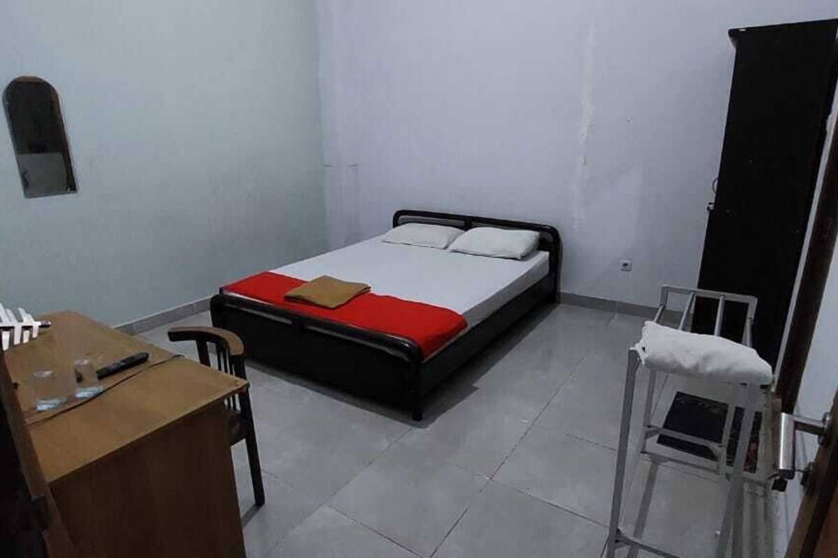 A small, sparsely furnished room with a single bed, a desk, and a chair.