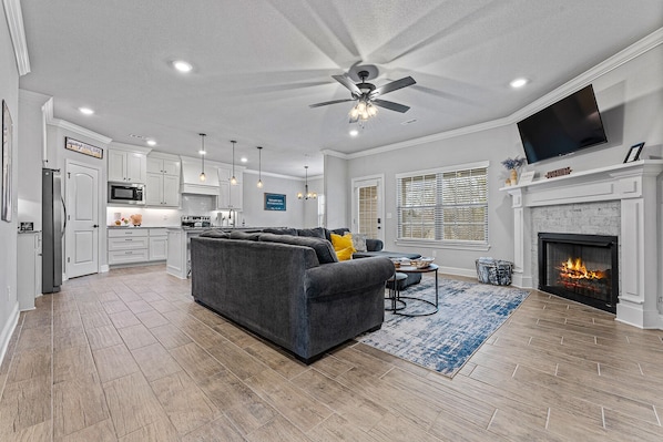 A spacious living room with a gray sectional sofa, a fireplace, and a ceiling fan.