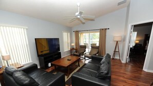 Ein Wohnzimmer mit Flachbildfernseher, Ledersofas, einem Couchtisch und einem Deckenventilator.