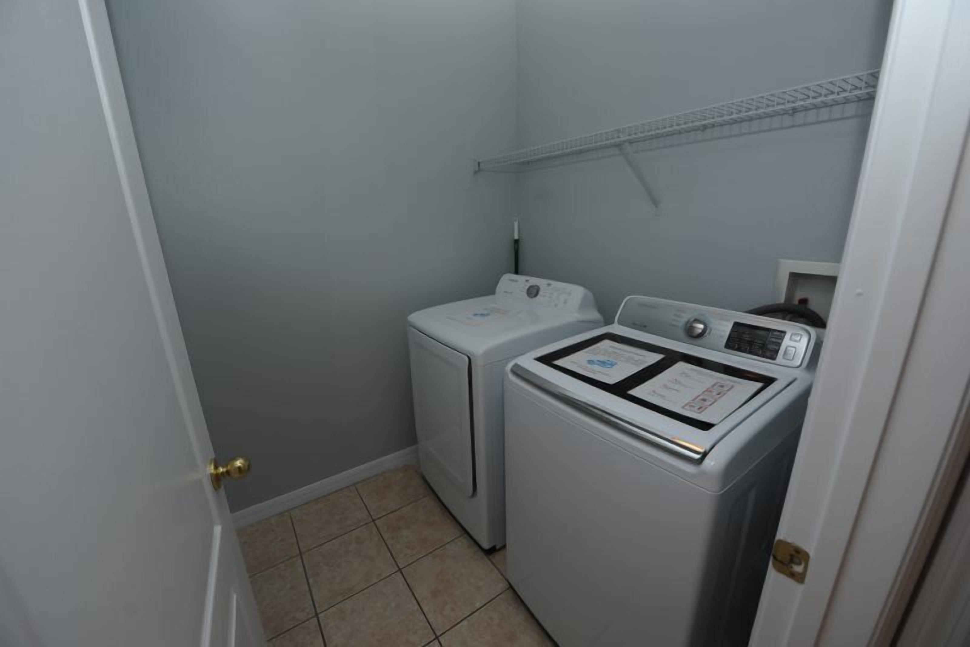 A laundry room with two white washing machines and a shelf above them.