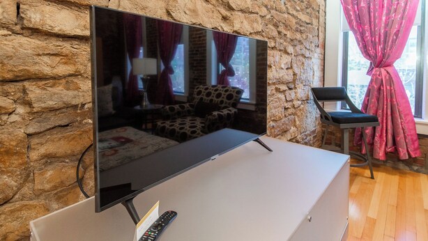 Un televisor de pantalla plana sobre un mueble blanco con un control remoto, frente a una pared de piedra.