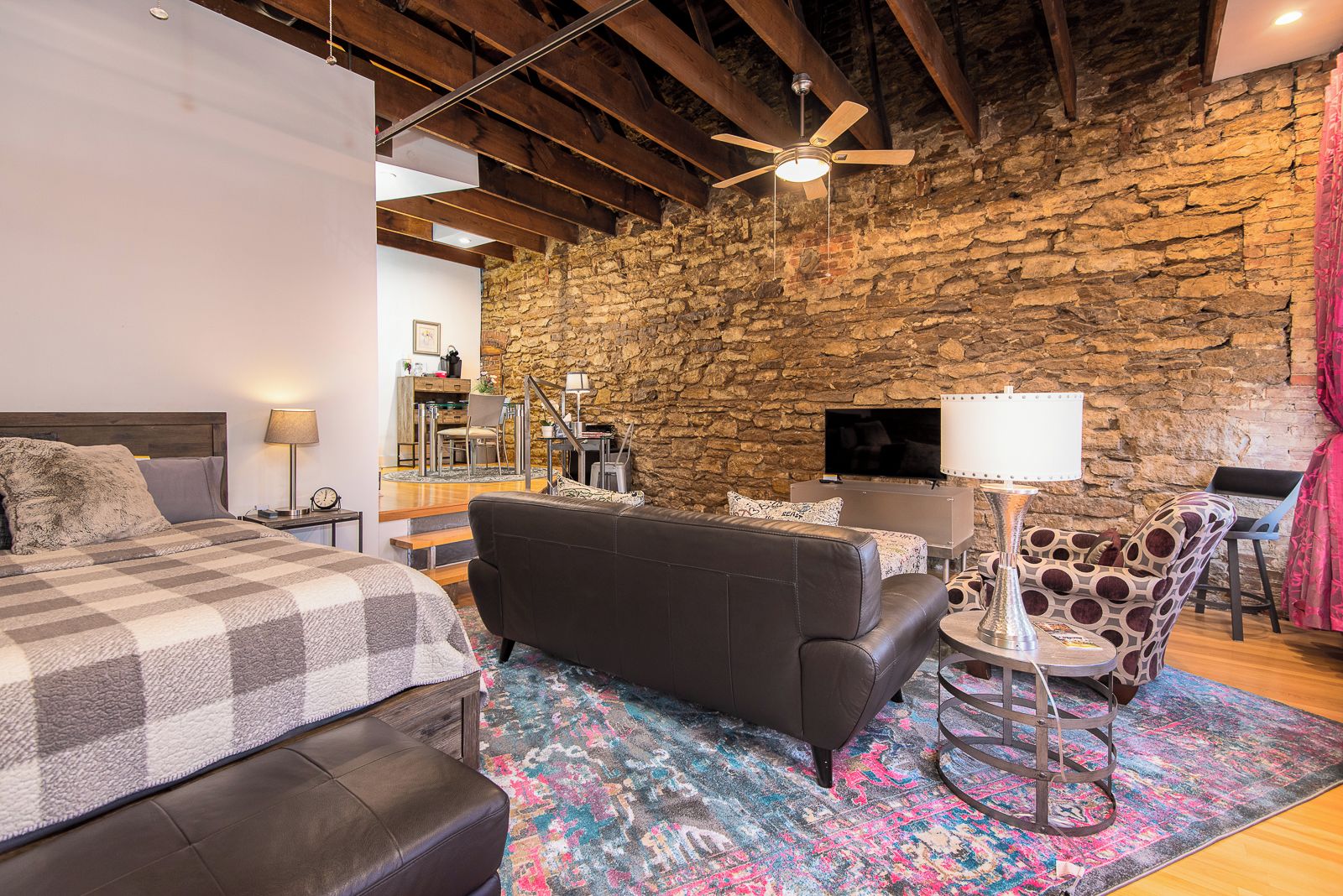 A bedroom with a bed, a sofa, a TV, a desk, and a stone wall.