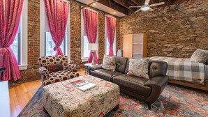 Una sala de estar acogedora con pared de ladrillo, un sofá de cuero, un reposapiés estampado y un sillón con estampado de lunares.