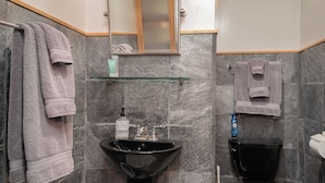 Un baño con un lavabo negro, un inodoro y un estante de vidrio con artículos de aseo.