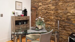 Un comedor con mesa de vidrio, sillas, pared de piedra y mueble de madera con utensilios de cocina.
