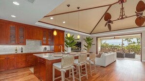 Una cocina moderna con armarios de madera, una isla central y una zona de comedor con sillas de mimbre.
