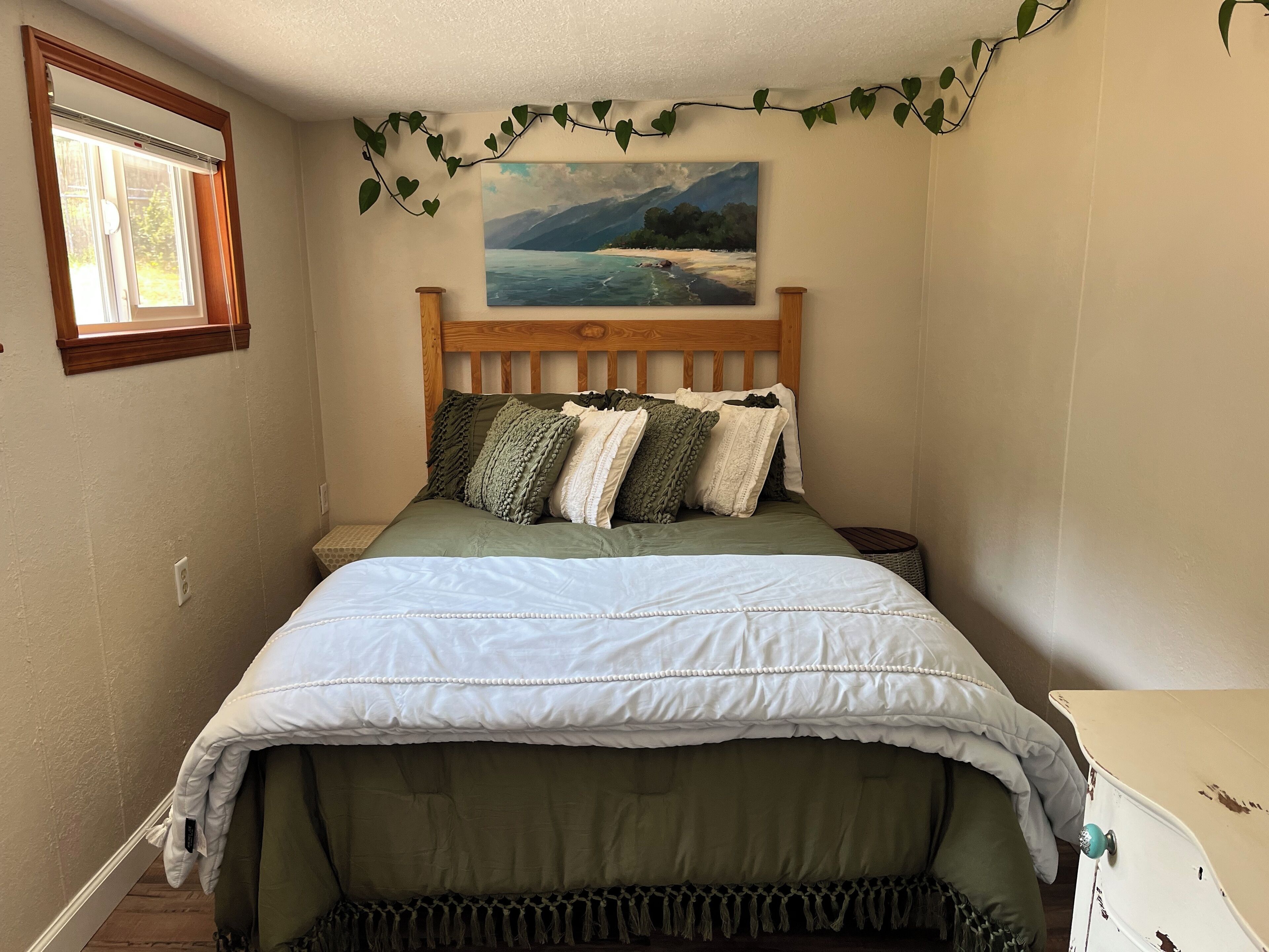 A bedroom with a wooden headboard, a painting of a beach scene, and a window with blinds.
