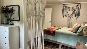 Ein Schlafzimmer mit Bett, Kommode, Wandbehang und einer Makramee-Vorhang.