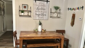 Una sala da pranzo con un tavolo e sedie in legno, due mensole a parete con oggetti decorativi e un pavimento in legno.