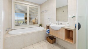 A modern bathroom with a bathtub, a sink, and a large mirror. - The Pool Resort - One Bedroom Pool & Ocean Views (Tweed)