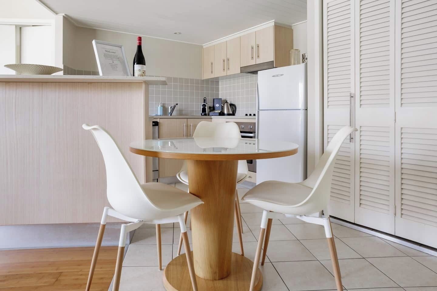 A modern kitchen with a round wooden table, two white chairs, and a white refrigerator.