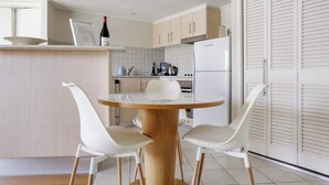 A modern kitchen with a round wooden table, two white chairs, and a white refrigerator. - The Pool Resort - 1BR Pool View Haven (KINGSCLIFF)