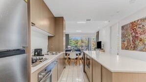 A modern kitchen with stainless steel appliances, a dining area with a view, and a large abstract painting on the wall.