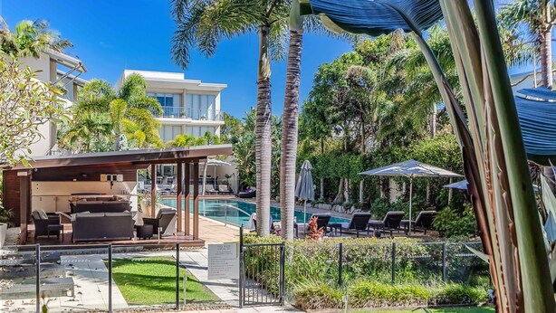 A poolside area with lounge chairs, a covered seating area, and a clear view of a modern building in the background.