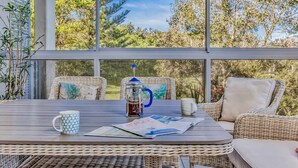 A covered outdoor seating area with wicker furniture, a coffee maker, and a magazine on a table.