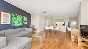Ein modernes Wohnzimmer mit einer grauen Couch, einem Glastisch und einem Essbereich mit weißen Stühlen.