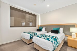 Habitación de hotel con dos camas, un ventanal grande, una mesita de noche con lámpara y un cabecero.