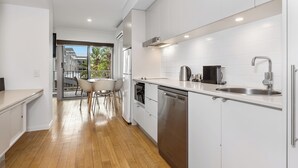 A modern kitchen with white cabinets, stainless steel appliances, and a wooden floor. - The Sand Resort Kingscliff - One Bed Pool view (3202) (Tweed)