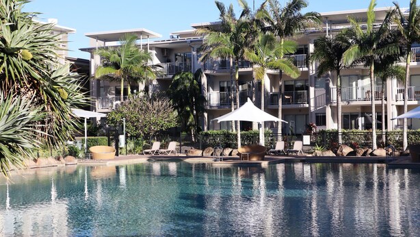 A hotel with a pool, lounge chairs, and palm trees. - The Sand Resort Kingscliff - One Bed Pool view (3202) (Tweed)