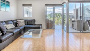 A modern living room with a leather sectional sofa, a glass coffee table, and a sliding glass door leading to an outdoor patio area. - The Sand Resort Kingscliff - One Bed Pool view (3302) (Tweed)