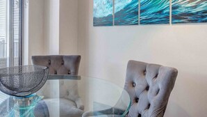 A modern dining area with a glass table, two grey upholstered chairs, a metal bowl centerpiece, and a large abstract painting on the wall. - The Sand Resort Kingscliff - One Bed Pool view (3302) (Tweed)