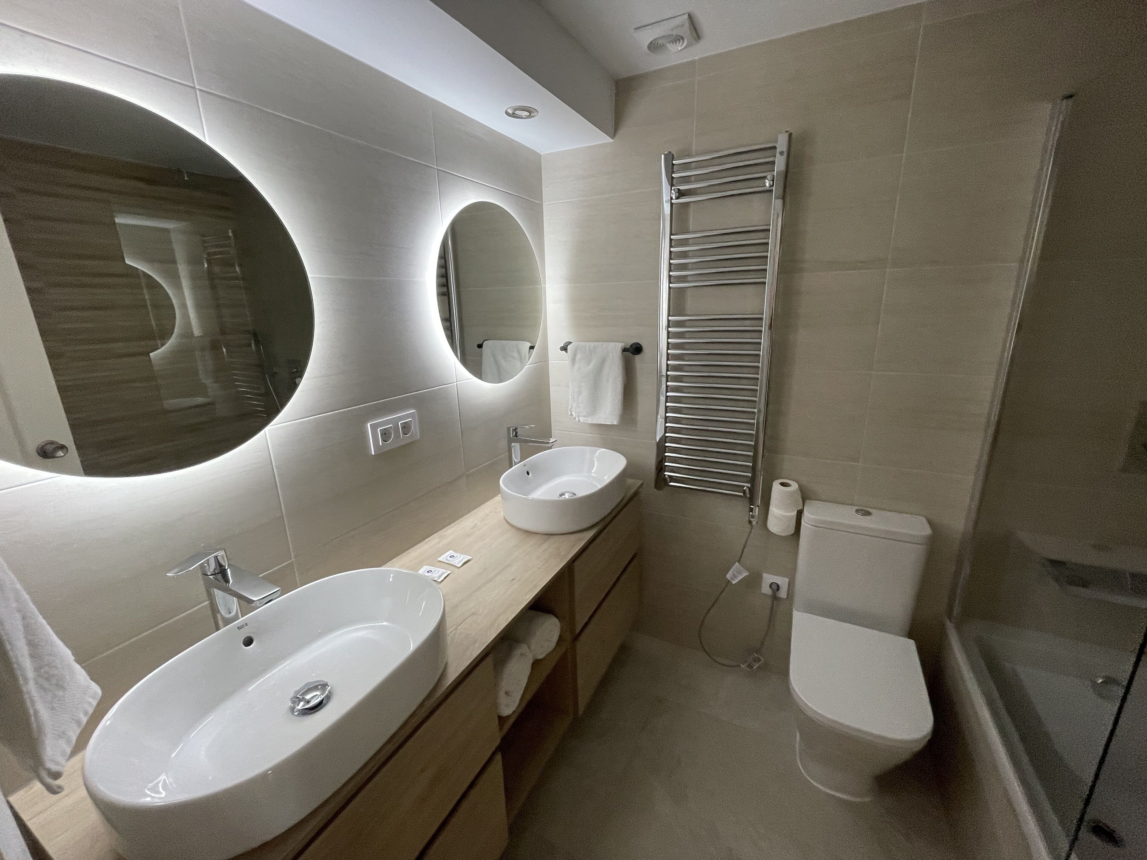 Un bagno moderno con due lavandini, uno specchio grande, un portascopevoli e una doccia.