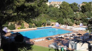 A swimming pool with lounge chairs and umbrellas, surrounded by trees and a building in the background. - 2 Bedroom Bellaluz Penthouse Apartment, La Manga Club (Cartagena)