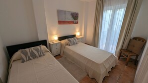 A hotel room with two beds, a nightstand with lamps, a chair, a window with curtains, and a wall-mounted painting. - 2 Bedroom Bellaluz Penthouse Apartment, La Manga Club (Cartagena)