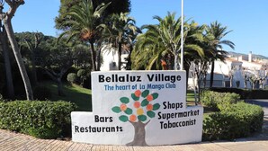 A sign for Bellaluz Village, highlighting its status as the heart of La Manga Club, with amenities including bars, restaurants, shops, a supermarket, and a tobacconist. - 2 Bedroom Bellaluz Penthouse Apartment, La Manga Club (Cartagena)