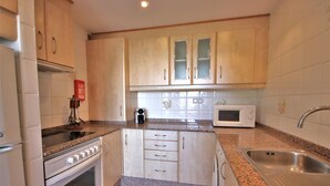 A compact kitchen with white cabinets, a built-in oven, a microwave, and a stainless steel sink. - 2 Bedroom Bellaluz Penthouse Apartment, La Manga Club (Cartagena)