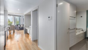 Un interior moderno con suelo de madera, un área de comedor con sillas y mesa, un sofá, y un baño con bañera y paredes con azulejos.