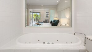 A modern bathroom with a large bathtub, a glass-enclosed shower area, and a view of a living room with a sofa and a coffee table. - The Sand Resort Kingscliff - Dual key 2B (6217/18) (Casuarina)