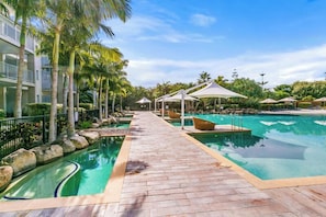 A pool area with a wooden deck, palm trees, and umbrellas. - The Sand Resort Kingscliff - Two Bed Dual Key Plunge Pool (Casuarina)