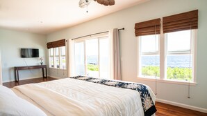 Ein Schlafzimmer mit einem großen Bett, einem Deckenventilator, einem Fernseher und Meerblick durch die Fenster.