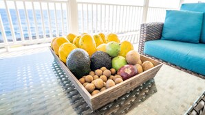 Ein hölzernes Obst- und Nussbrett auf einem Glastisch mit Blick auf das Meer und einem blauen Sofa im Hintergrund.