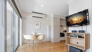 A modern kitchen with a flat-screen TV mounted on the wall, a dining area with a table and chairs, and a large window providing natural light. - The Sand Resort Kingscliff - One Bed Spa Suite (8302) - Holiday Management Co. (Tweed)