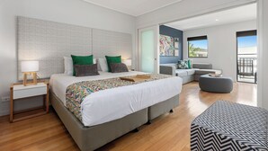 A modern bedroom with a large bed, a nightstand, a grey sofa, and a balcony with a view.
