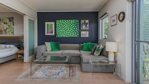 En moderne stue med en grå sofa, grønne puder, et glasbord og et mønstret gulvtæppe.
