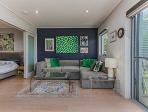 A modern living room with a grey sofa, green cushions, a glass coffee table, and a patterned rug.