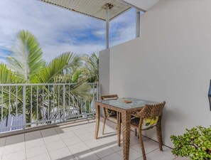 A balcony with a table and chairs, surrounded by white walls and a view of palm trees.