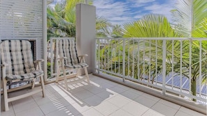 En balkon med to fletstole, gelænder i hvidt og udsigt til palmer og en klar himmel.