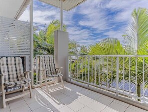 Un balcon avec deux fauteuils en osier, une balustrade blanche et une vue sur des palmiers et un ciel dégagé.