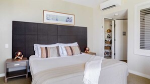 Un dormitorio con una cama grande, dos mesitas de noche, un aire acondicionado instalado en la pared y un cuadro enmarcado sobre la cama.