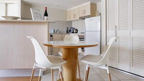 Una cocina moderna con una mesa redonda de madera, dos sillas blancas y un refrigerador blanco.