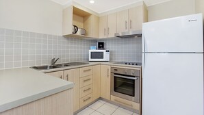 Eine moderne Küche mit hellen Holzschränken, einer Edelstahl-Spüle, einer Mikrowelle, einem Backofen und einem weißen Kühlschrank.
