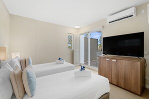 Two single beds with white linens and blue patterned pillows, a flat-screen TV, and sliding glass door to an outdoor area.