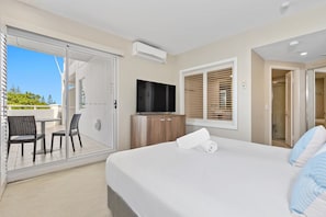 Relax in a serene space with a large bed, flat-screen TV, and sliding glass door to a balcony with a table and chairs.
