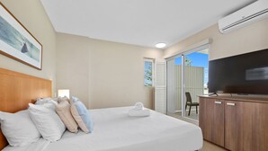 A hotel room with a large bed, a flat-screen TV, a wooden headboard, a balcony with a chair, and an air conditioning unit. - North facing park view 2bed2bath - WIFI + parking (Casuarina)