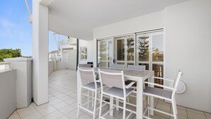 A clean, white outdoor patio with a dining table and chairs, large windows, and a tiled floor. - North facing park view 2bed2bath - WIFI + parking (Casuarina)